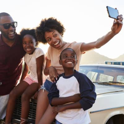 Family Posing For Selfie Next To Car Packed For Road Trip