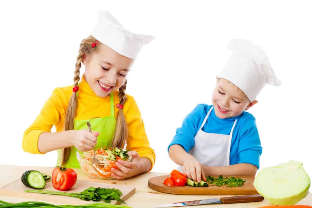 two kids in chef hats making a salad