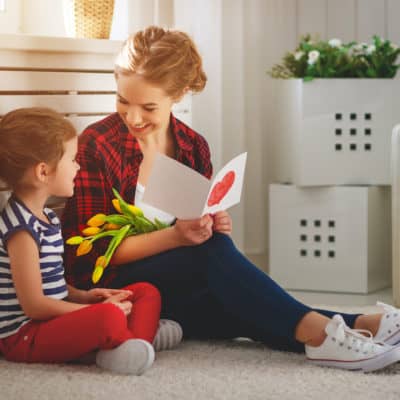 little girl giving flowers and card to her mom on mothers day