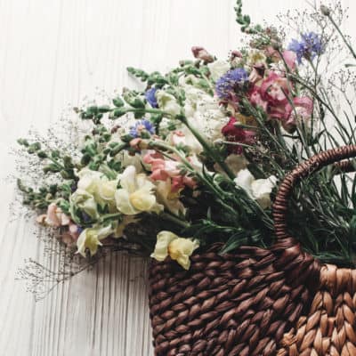 beautiful woven basket filled with wildflowers on a white wood background