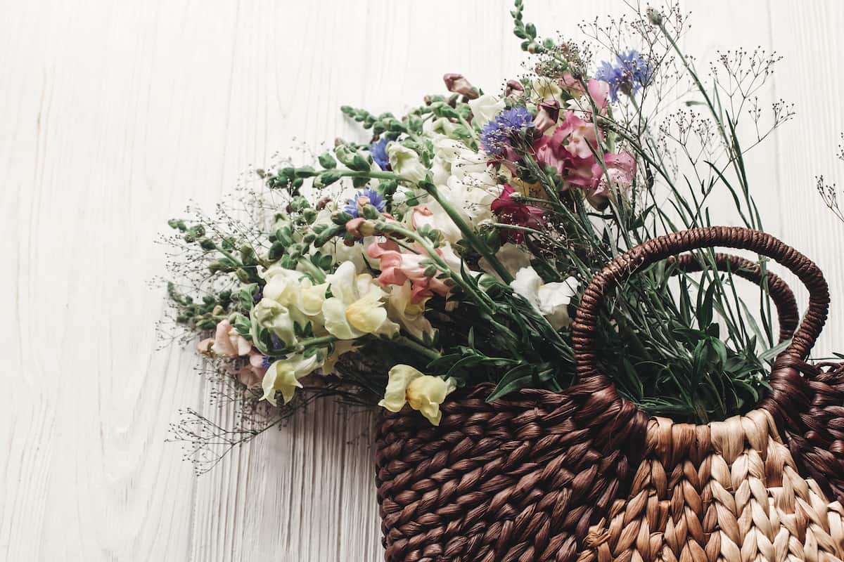 beautiful woven basket filled with wildflowers on a white wood background