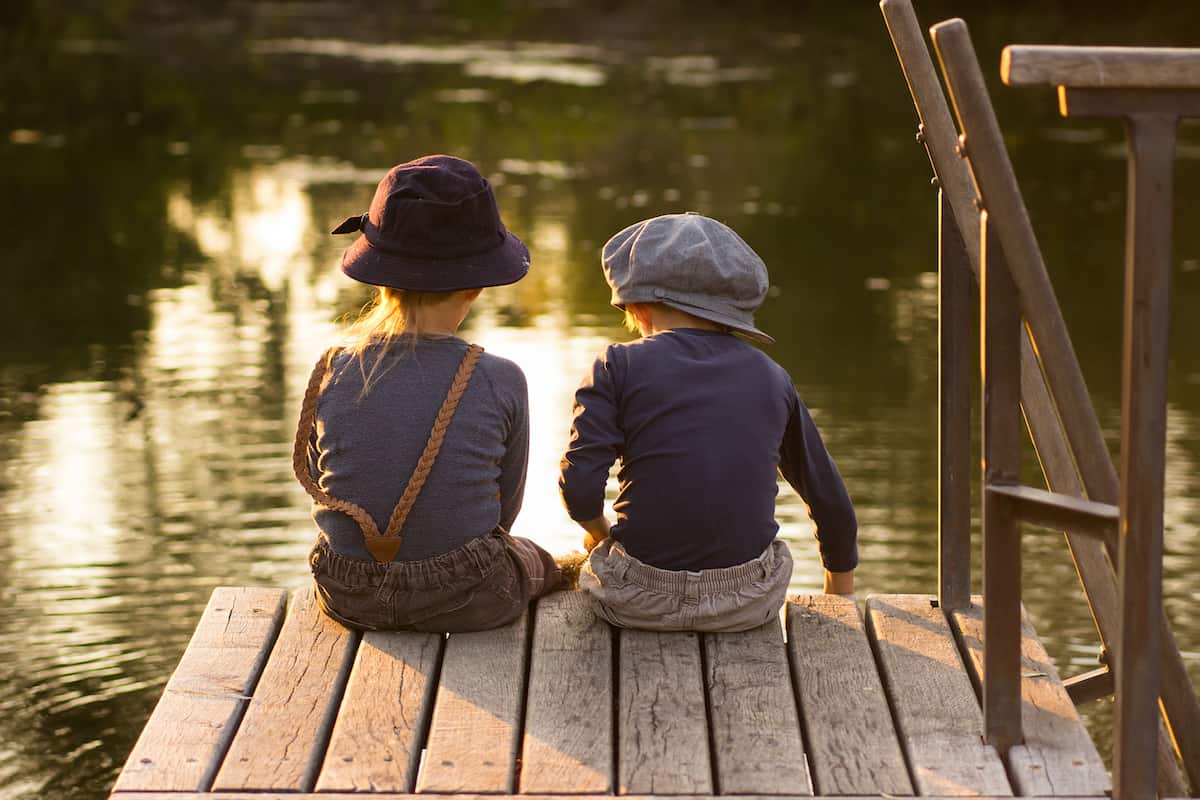 two kids sitting on a dock fishing 