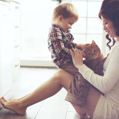 Mother with her baby playing with pet on the floor at the kitchen at home