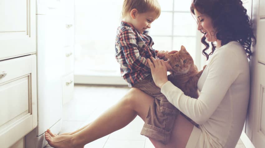 Mother with her baby playing with pet on the floor at the kitchen at home