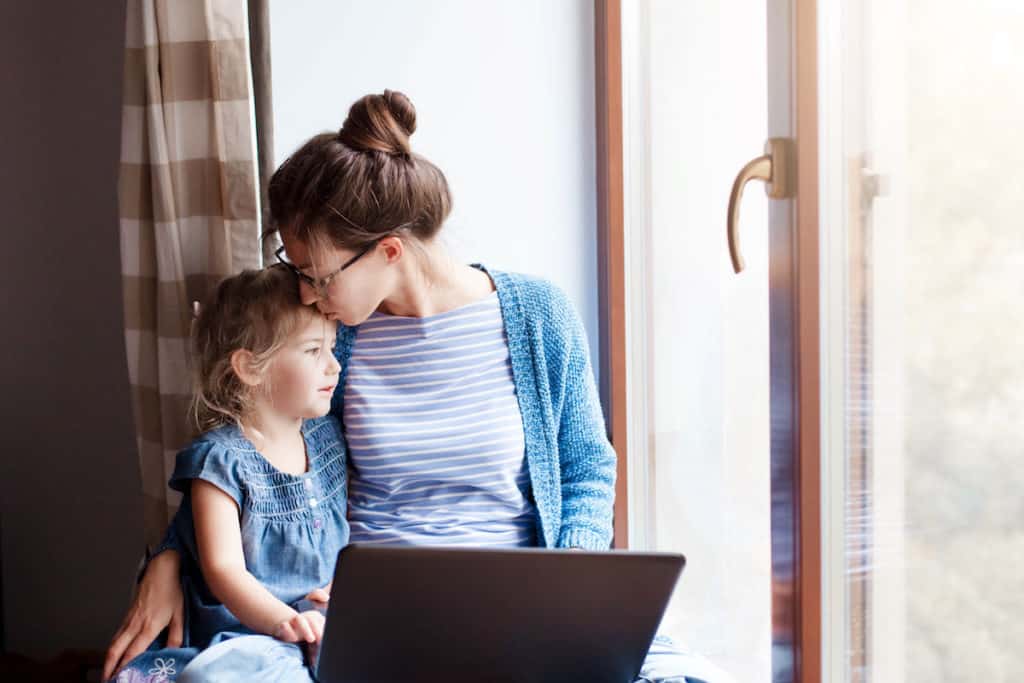 Mother working on computer holding daughter.