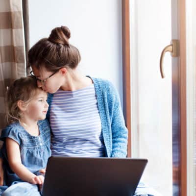 Mother working on computer and holding daughter.