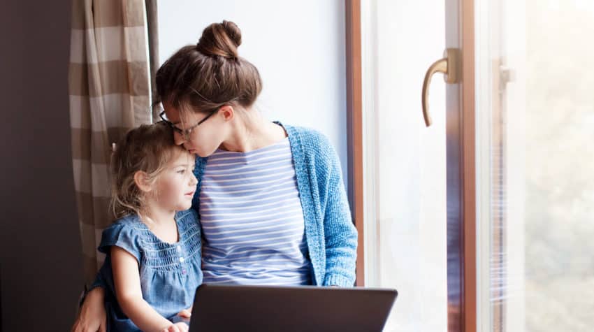 Mother working on computer and holding daughter.