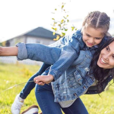 smiling mom giving daughter a piggyback ride outside