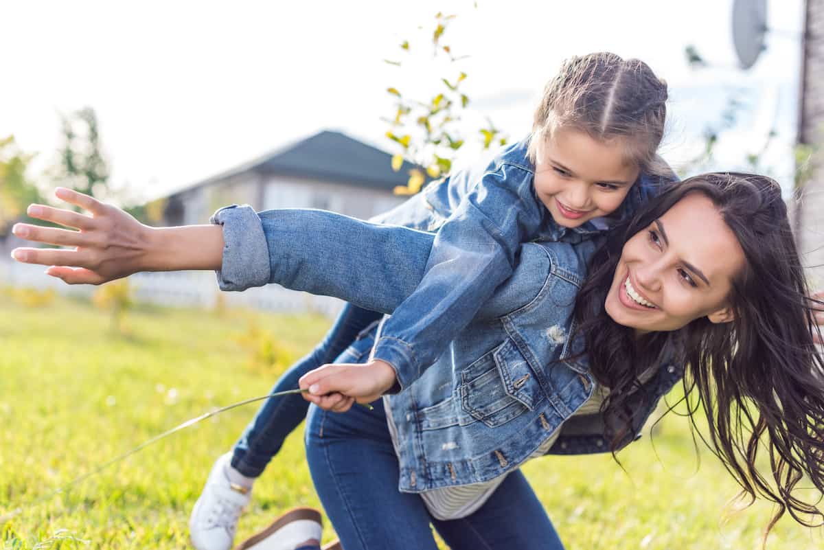 Mom smiling as she gives her daughter a piggyback ride outside