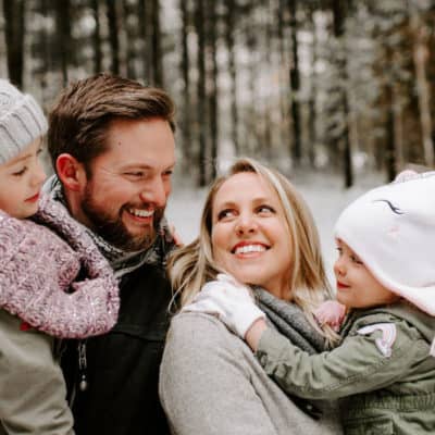 family of 4 smiling at each other in the snow